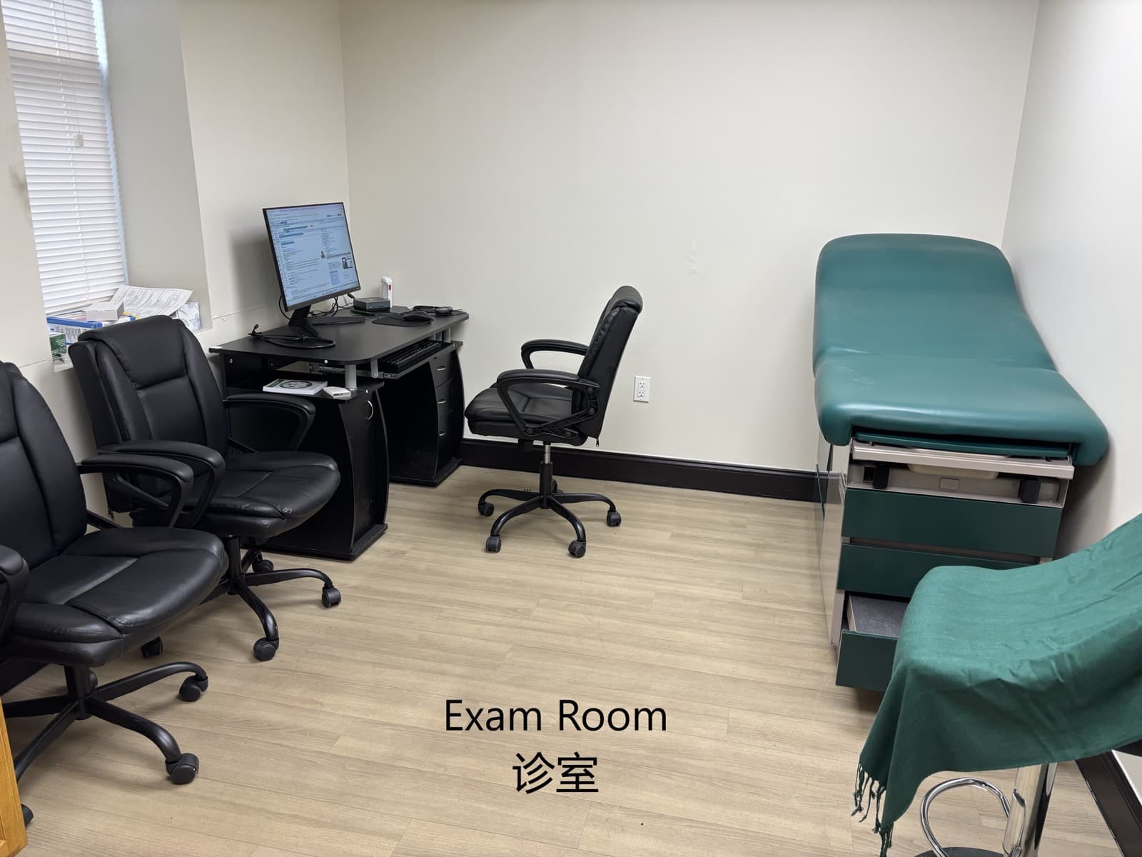 A clinic exam room with a green examination bed and a computer workstation