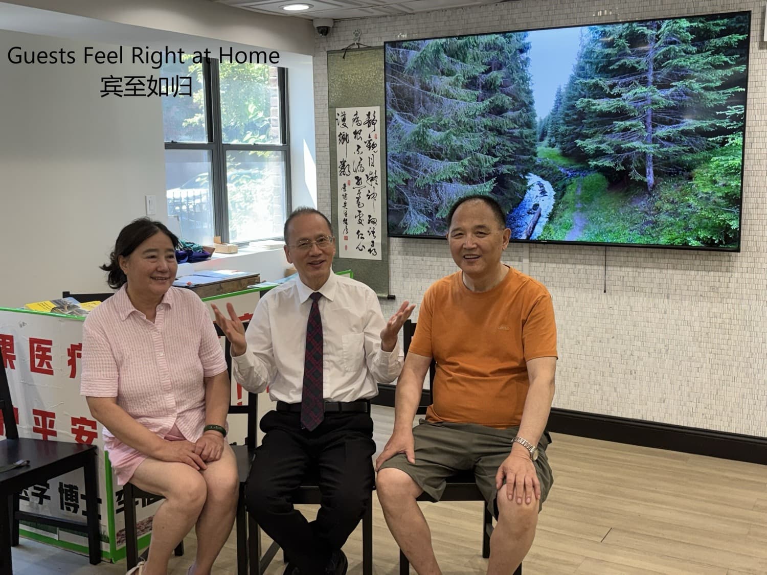 Dr. Lee talking with two guests seated in front of a large screen showing forest scenery and a calligraphy scroll